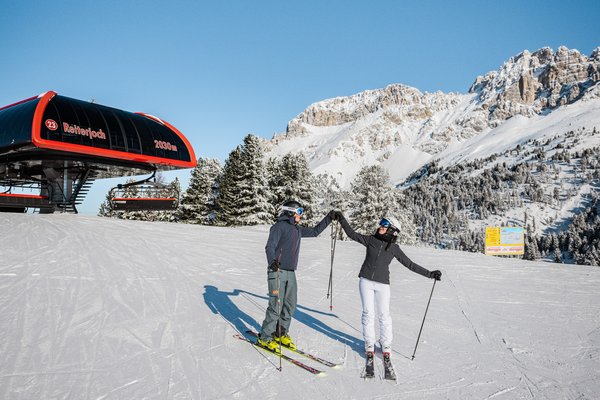 Zwei Skifahrende klatschen mit den Händen ein, Lift im Hintergrund